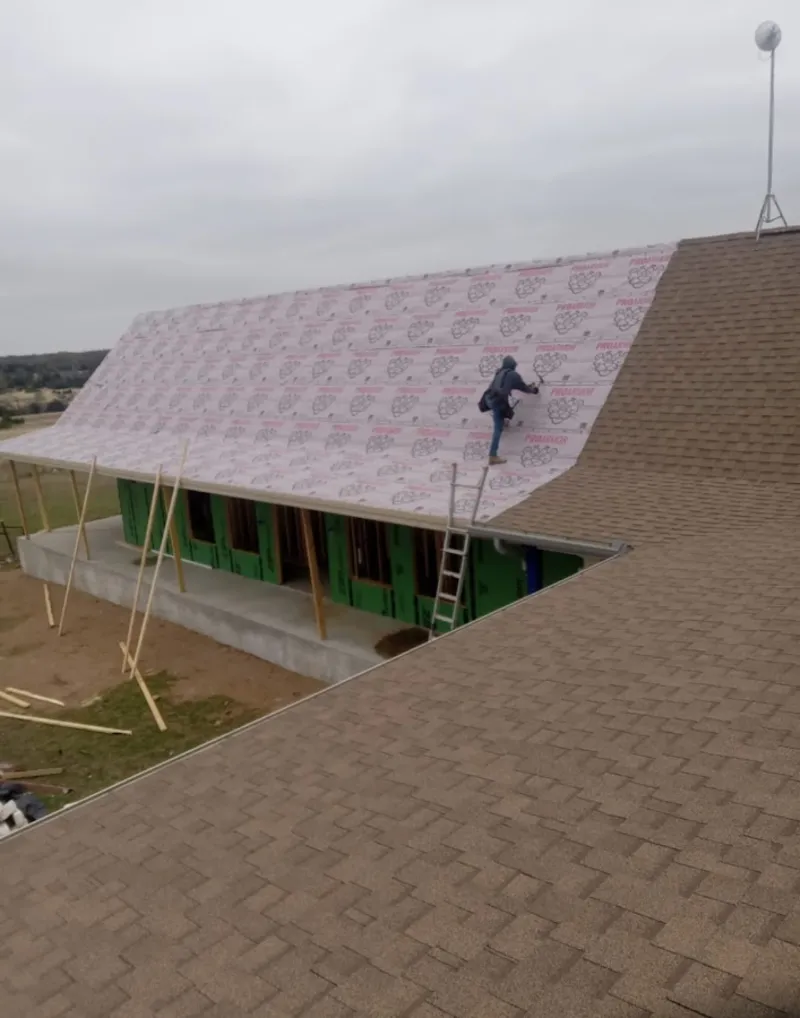 Worker preparing underlayment for a metal roof installation in Adel